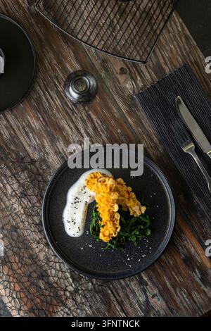 Knusprig gebratene Fischstäbchen auf einem Bett aus Spinat mit cremiger weißer Sauce und schwarzen Sesamsamen Stockfoto