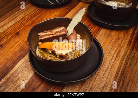 Schichtkuchen mit Schokolade und Orangenscheibe, serviert in einer dunklen Schüssel auf einer Holzoberfläche, saftiger Schokoladenkuchen Stockfoto