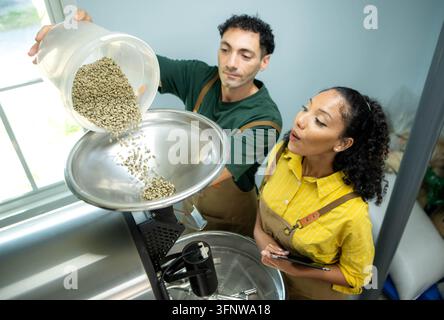 Kaffeeprofis laden frische grüne Kaffeebohnen in eine kommerzielle Röstmaschine, bevor der Röstprozess beginnt Stockfoto