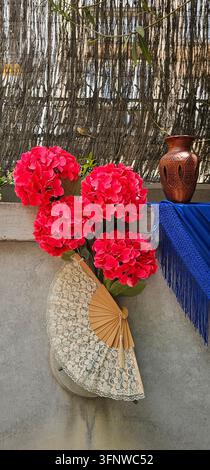 Rote Blumen, Spitzenhandfächer und Fransentextil in einer Cruces de Mayo-Dekoration in Granada, Spanien, am 4. Mai 2025. Stockfoto
