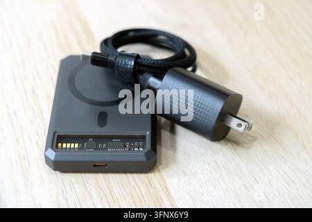 Eine magnetische drahtlose Powerbank gepaart mit einem Schnellladeadapter und USB-Kabel auf einem hellen Holz Hintergrund. Stockfoto