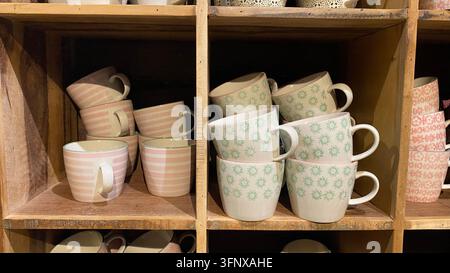 Bunte gemusterte Keramik-Kaffeetassen, die auf Holzregalen in einem Wohndeko-Shop angeordnet sind Stockfoto