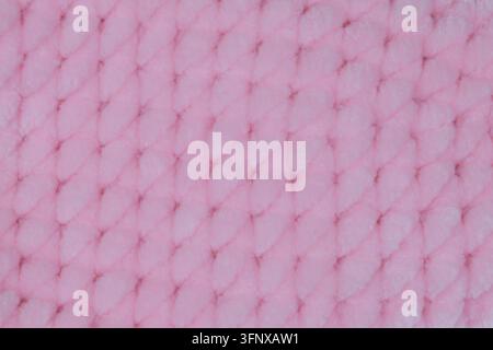 Vollformat-Textur aus weichem rosa gestricktem Plüschstoff mit geometrischem Diamant-Maschenmuster, ideal für Babydecke, Textil-Mockup oder Hintergrund. Stockfoto