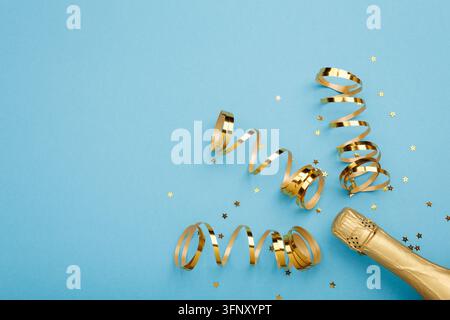 Festlicher Flat Lay mit goldenen Bandspiralen, Champagnerflasche und Sternkonfetti auf blauem Hintergrund zur Feier von Weihnachten und Neujahr. Stockfoto