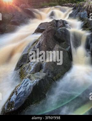 Kaskadierender Wasserfall fließt über dunkle, gezackte Felsen nahe Ruskeala, Karelien, Russland, und erzeugt einen sanften, weißen Nebel. Das Wasser erscheint seidig aufgrund langer Belichtung Stockfoto