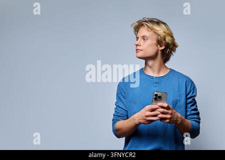 Junger Mann hält ein Smartphone und schaut weg im Studio-Porträt Stockfoto
