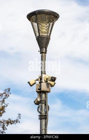 Eine Nahaufnahme zeigt einen metallenen Straßenlaternenmast, der mit Überwachungskameras ausgestattet und mit Spinnweben bedeckt ist, vor einem hellen Taghimmel. T Stockfoto