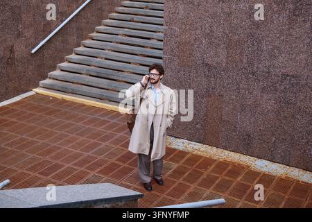 Ein junger, gutaussehender Geschäftsmann steht im Freien in einem schicken Outfit und führt ein Telefongespräch. Stockfoto