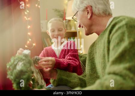 Senior Mann und Mädchen schmücken einen Weihnachtskranz zu Hause Stockfoto