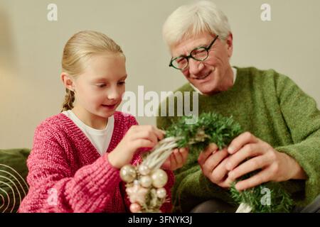 Senior Mann und Mädchen schmücken einen Weihnachtskranz zu Hause Stockfoto