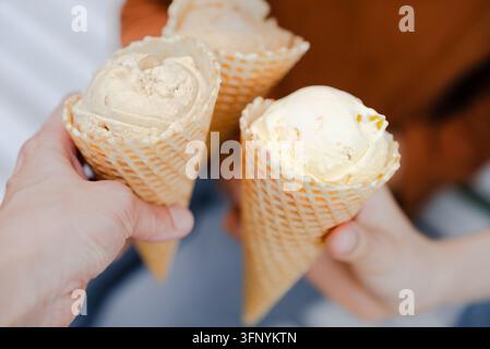 Menschliche Hände halten süße Waffeltüten gefüllt mit köstlichen Leckereien an einem sonnigen Sommertag. Freunde teilen Glück und Wärme, während sie diese köstlichen Snacks zusammen im Freien genießen. Stockfoto