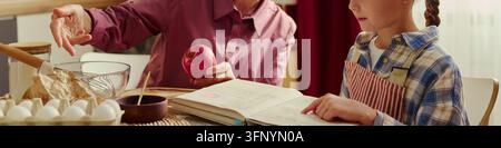 Kopf einer Mädchen, das ein Kochbuch liest, mit einer älteren Frau, die einen frischen Apfel hält Stockfoto