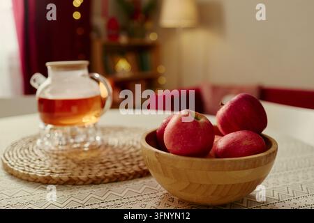 Frische rote Äpfel in einer Schüssel und Kräutertee auf dem Tisch zu Hause Stockfoto