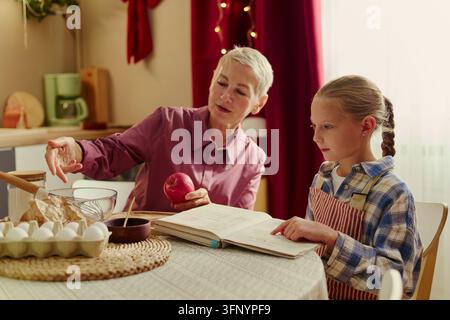 Seniorin und Mädchen lesen Rezeptbuch beim Backen in der Küche Stockfoto