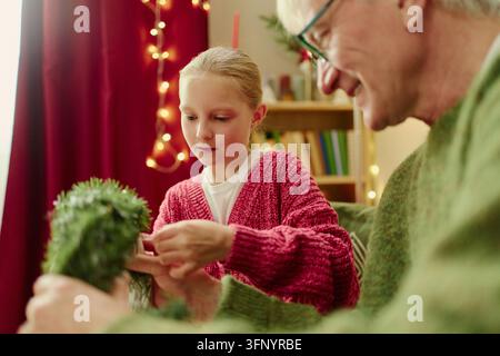 Mädchen mit Senior Mann dekoriert Weihnachtskranz zu Hause Stockfoto