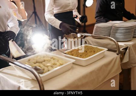 Catering-Teammitglieder in Uniformen servieren warme Speisen von Buffet-Trays bei einer Veranstaltung, mit professionellem Service und Atmosphäre, Catering-Fachteam Stockfoto