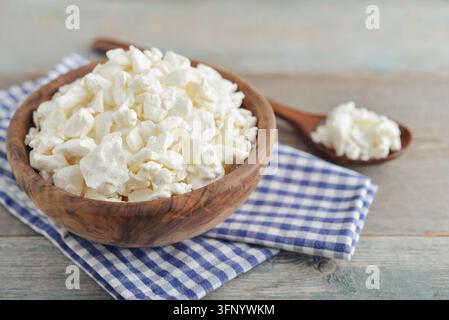 Kottagekäse in einer Holzschüssel mit einem Holzlöffel und einer karierten Stoffserviette auf einem rustikalen Holzgrund, Nahaufnahme Stockfoto