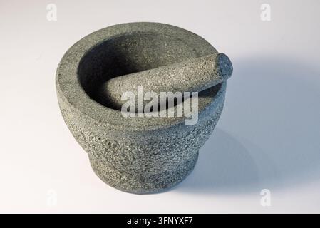 Ein grauer Steinmörser und Stößel ist auf einem weißen Hintergrund dargestellt. Der Stößel ruht im Mörser. Stockfoto