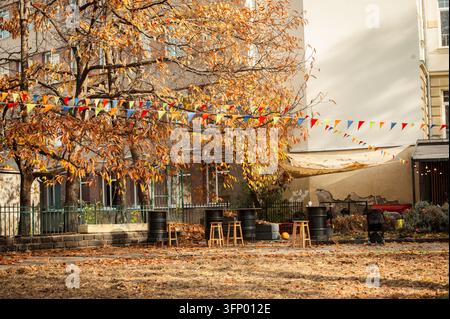 Straßenansicht eines Freiluft-Café-Balkons mit Tischen unter goldenen Herbstbäumen in einem historischen Stadtviertel. Gemütliche Stadtlebensart, Cafété Atmosphäre Stockfoto