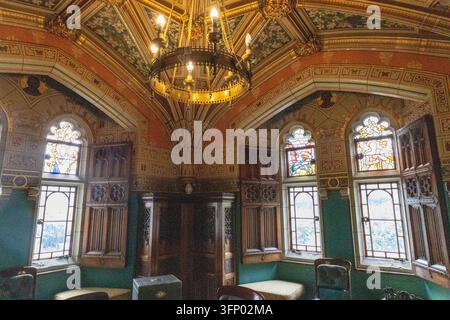 Prunkvoller historischer Raum in Cardiff Castle mit einem großen Kronleuchter, Buntglasfenstern, geschnitzter Holzvertäfelung, dekorativen Deckenmustern und Polsterung Stockfoto