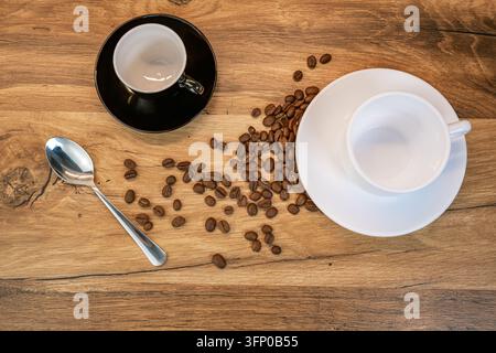 Überkopf-Arrangement von zwei leeren Kaffeetassen, gerösteten Bohnen und einem Teelöffel auf einer warmen Holzoberfläche mit großzügigem Kopierraum Stockfoto