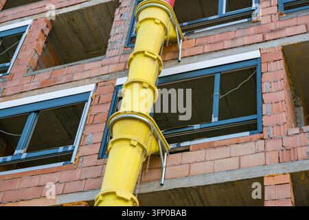 Gelbe Bauschuttreinigung an einem unfertigen Ziegelgebäude mit freiliegenden Betonböden, Fensterrahmen, Ketten und Metallstützen Stockfoto