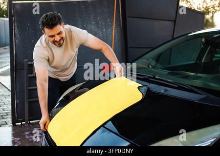 Mann trocknet schwarzes Auto mit Mikrofaser-Tuch Stockfoto