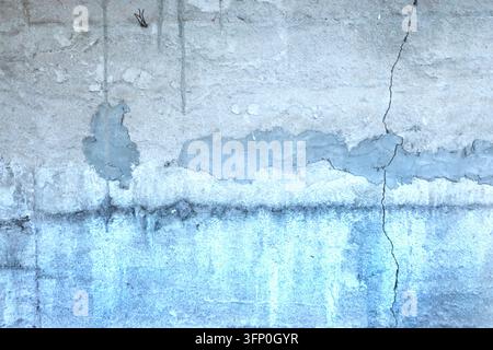 Vollbild-Hintergrund einer alten Betonoberfläche mit blasshellblauer Färbung, auffälligem vertikalem Riss, grauen Zementflecken und verwittertem industriellem Schmutz Stockfoto