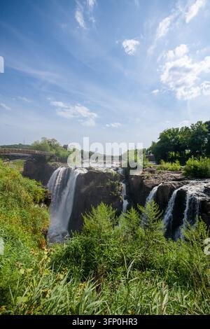Luftaufnahme der Paterson Great Falls, die über felsige Klippen stürzen, umgeben von üppigem grünen Blattwerk und Bäumen unter einem strahlend blauen Himmel in New Jersey, Uni Stockfoto
