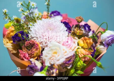 Eine Nahaufnahme eines alten verblassten Blumenstraußes mit einem verschrumpelten rosa Chrysanthemum und bunten welken Rosen. Verwitterte trockene Blumenkomposition Stockfoto