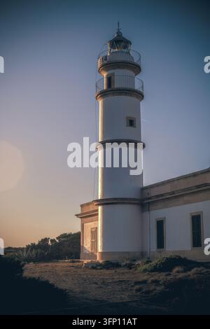 Eine niedrigwinklige Vertikalaufnahme des Faro de Cap Salines Leuchtturms in Mallorca, Spanien, während des Sonnenuntergangs. Der weiße Turm erhebt sich hoch gegen einen Gradientenhimmel Stockfoto