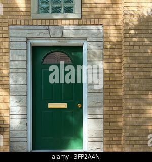 Greentür mit einem halbrunden Fenster steht in einem steinernen Rahmen gegen gelbe Ziegelsteine. Stockfoto