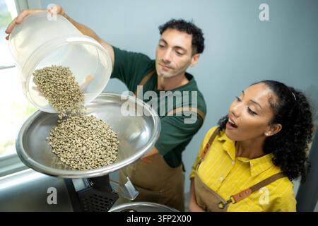 Kaffeeprofis laden frische grüne Kaffeebohnen in eine kommerzielle Röstmaschine, bevor der Röstprozess beginnt Stockfoto