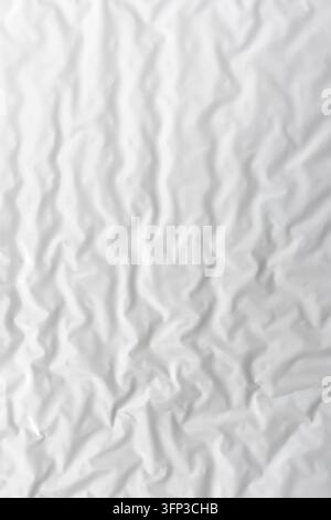Weißes zerknittertes Papier füllt das Bild mit sanften Falten, subtilen Schatten und einer unebenen Oberfläche und schafft eine minimale monochromatische Textur, die für Hintergründe geeignet ist, ov Stockfoto