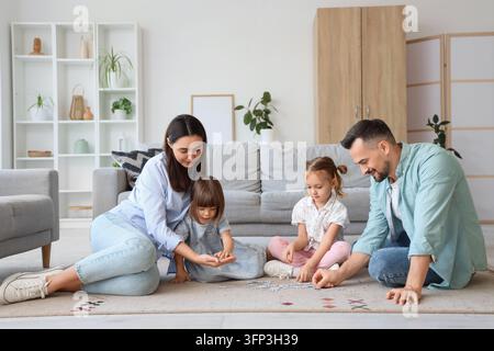 Familienbindung und Kindesentwicklung, Eltern und Kinder spielen mit einem Puzzle auf dem Wohnzimmerboden für Qualitätszeit und Heimunterricht Stockfoto