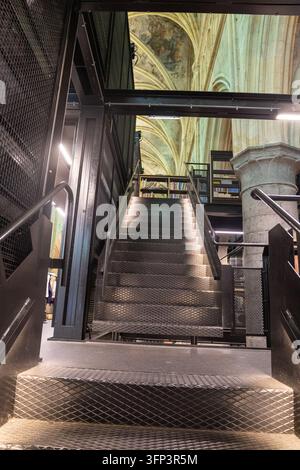 Innenraum des Boekhandel Dominicanen in Maastricht, zeigt eine schwarze Metalltreppe und Bücherregale unter gotischen Kreuzrippengewölben mit historischer Wandmalerei Stockfoto