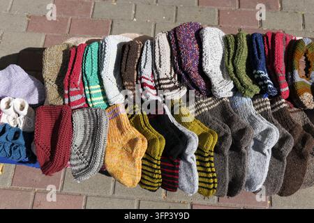 Handgestrickte bunte Wollsocken werden zum Verkauf auf einem Ziegelpflaster ausgestellt, verschiedene Muster und Farbtöne sind zu sehen, die handgefertigte Kunsthandwerk repräsentieren und Wa Stockfoto