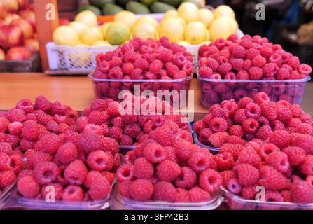 Reife rote Himbeeren werden sorgfältig in durchsichtigen Plastikbehältern angeordnet, was eine lebhafte Auslage auf einem Holztisch auf einem lokalen Bauernmarkt schafft, mit Stockfoto