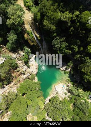 Vertikale Luftaufnahme von oben, die ein lebendiges grünes Flussbecken zeigt, umgeben von dichten Wald Bäumen und Felsen in Griechenland. Stockfoto