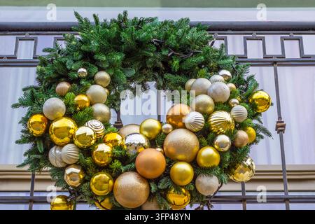Weihnachtskranz aus Fichtenzweigen und Goldbällen auf einem Gebäudebalkon. Stockfoto