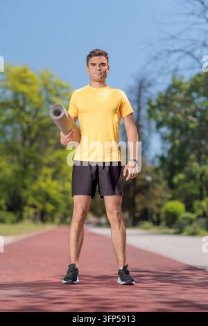 Junger Mann hält eine Yogamatte auf einer Laufbahn in einem Park Stockfoto