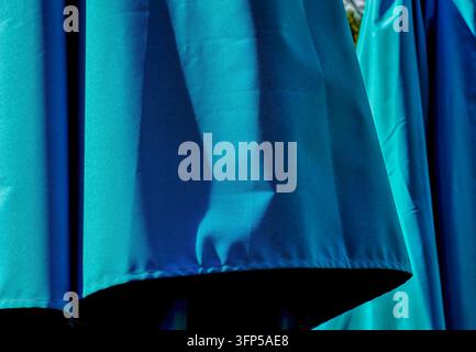 Ein lebendiger teal-farbener Stoff mit einer glatten Textur und weichen Falten, der im Sonnenlicht hinunterhängt. Stockfoto