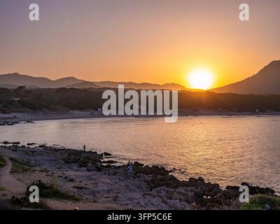 Die mediterrane Küstenbucht verwandelt sich während der Sonnenuntergangsstunde in Cala Rajada, Mallorca, in ein goldenes Paradies. Felsküste und bergiger Hintergrund schaffen Stockfoto