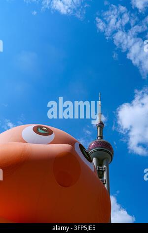 SHANGHAI, CHINA - 5. Okt. 2026: Niedrige Blickwinkelansicht des Oriental Pearl TV-Turms hinter einer riesigen aufblasbaren Cartoon-Installation vor einem klaren blauen Himmel Stockfoto