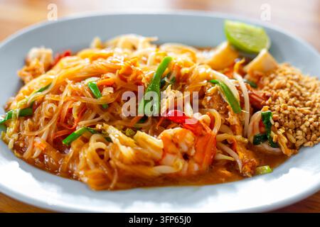 Teller mit traditionellen thailändischen Pad-Thai-Nudeln mit Garnelen und Limette auf einem Holztisch. Köstliche asiatische Küche und Street Food. Stockfoto
