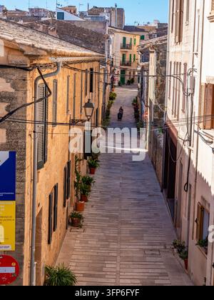 Eine steingepflasterte Treppe windet sich durch die historische Altstadt von Alcudia mit verwitterten Sandsteingebäuden, grünen Fensterläden und Terrazzodächern, die Stockfoto