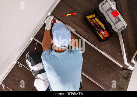 Oberblick auf einen Elektriker, der neben hölzernen Treppenstufen an der Verkabelung arbeitet, mit einem offenen Werkzeugkasten und isolierten Werkzeugen auf den Stufen. Stockfoto