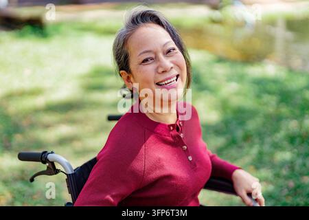 Zufriedene Seniorin lächelt, während sie im Rollstuhl sitzt, glückliche psychische Gesundheit Stockfoto