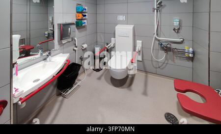 Helsinki, Finnland - 28. August 2026: Ein barrierefreies Krankenhaus-Badezimmer mit einer modernen Toilette mit roten Stützschienen, einem Waschbecken, einem Duschbereich, einem Stockfoto