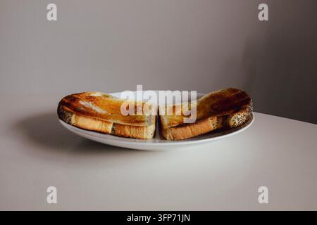 Zwei Scheiben goldbrauner Toast mit Butter und Mohn auf einem weißen Teller Stockfoto
